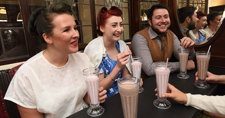 two women and man smiling whilst drinking milkshakes dressed in 1950s style fashion at Beamish Museum